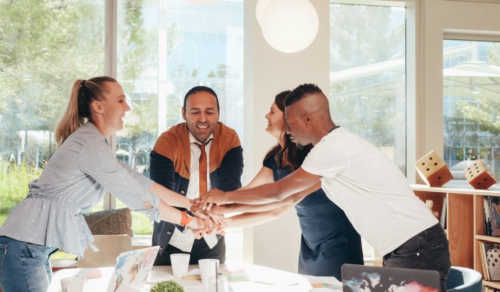 smiling multiracial coworkers with hands together in office