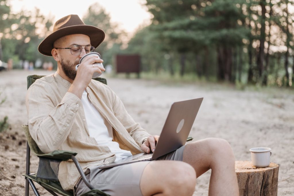 man in brown dress shirt and brown cowboy hat sitting on gray chair using macbook during